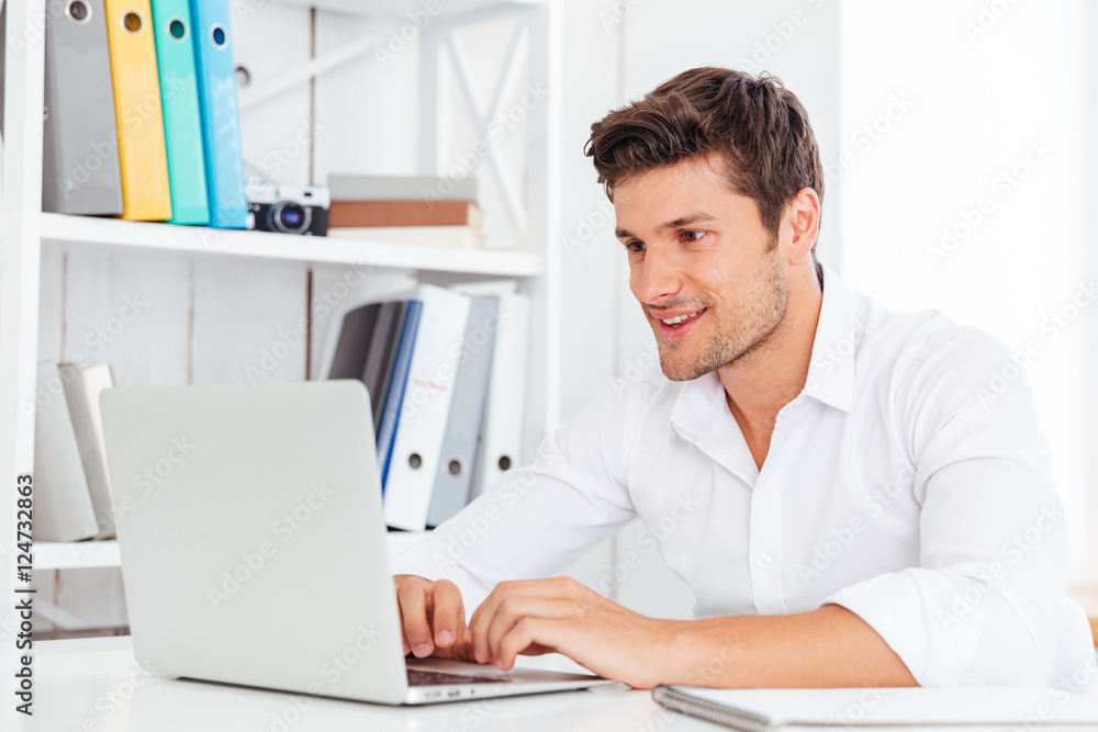 Smiling young happy businessman using laptop computer Smiling young happy businessman using laptop computer