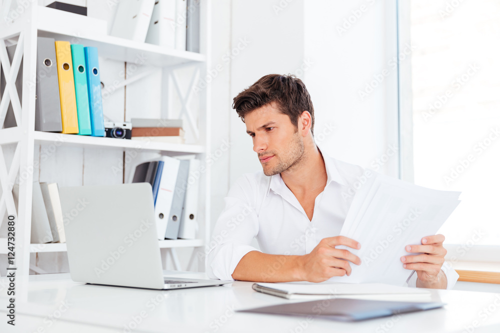 Handsome young businessman working with documents and laptop Handsome young businessman working with documents and laptop