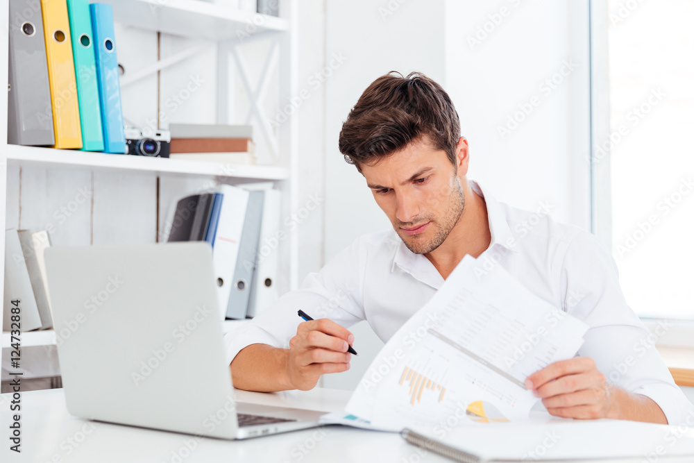 Obraz premium Concentrated young businessman sitting and writing at the table