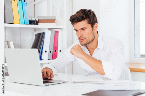 Handsome businessman sitting at the desk and using laptop © Drobot Dean