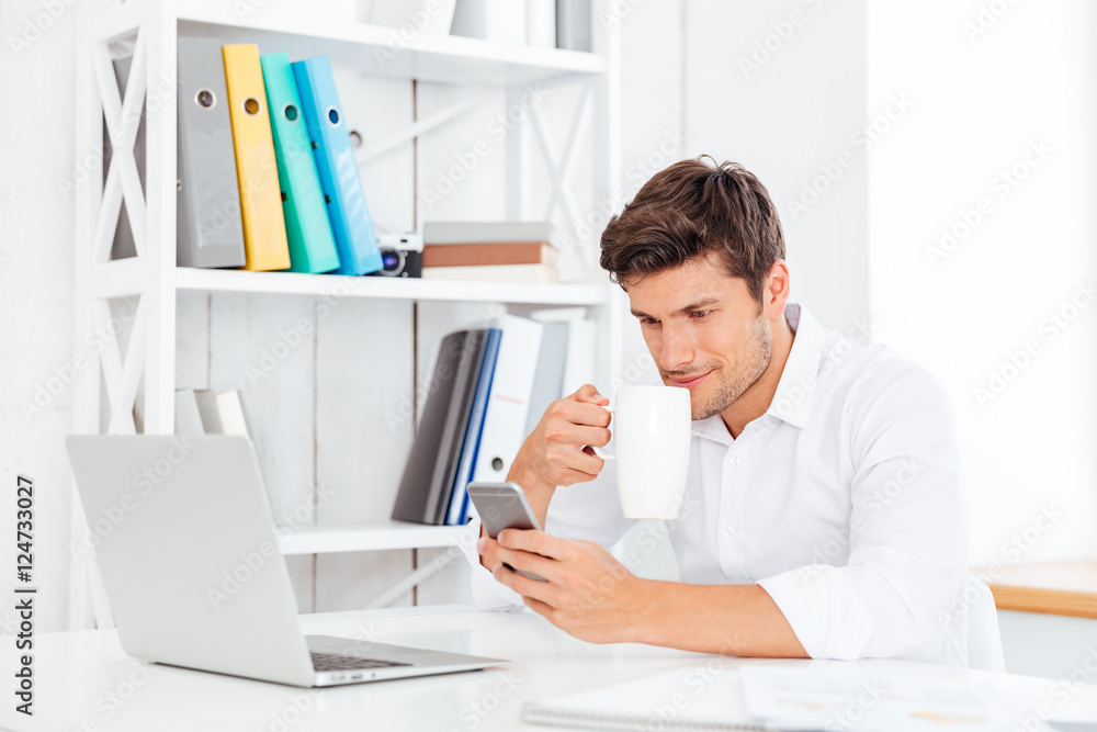 Cheerful young businessman drinking coffee and talking on mobile phone