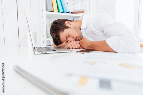 Exhausted fatigued young businessman sleeping on the table