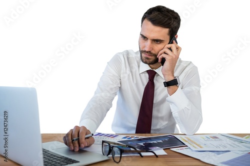 Businessman talking on mobile phone while working on laptop photo