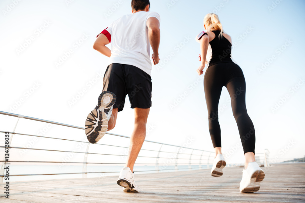 Back view of a young couple jogging at beach pier