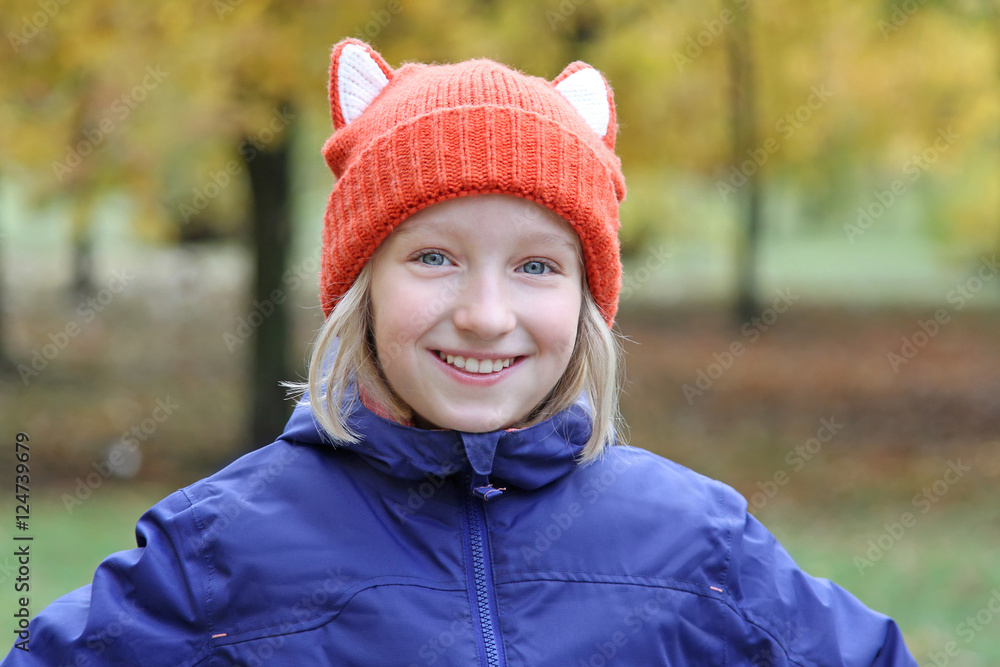 Cheerful girl smiling in a funny knitted cap with ears in the form of a fox. Autumn, outdoors. Cheerful girl smiling in a funny knitted cap with ears in the form of a fox. Autumn, outdoors.