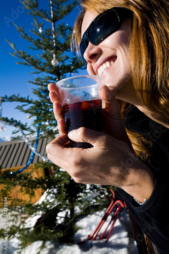 femme souriant qui boit du vin chaud sur une terrasse en hiver dans la neige