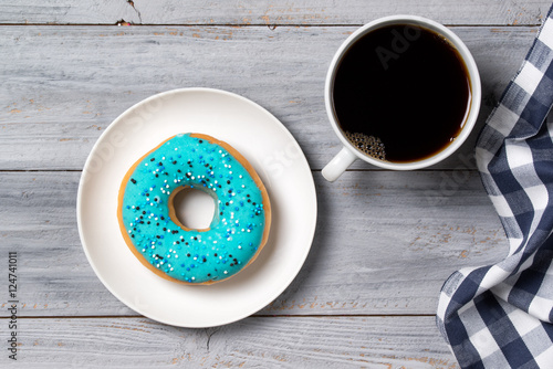 Blue donut decorated with sprinkles and cup of coffee, wooden background