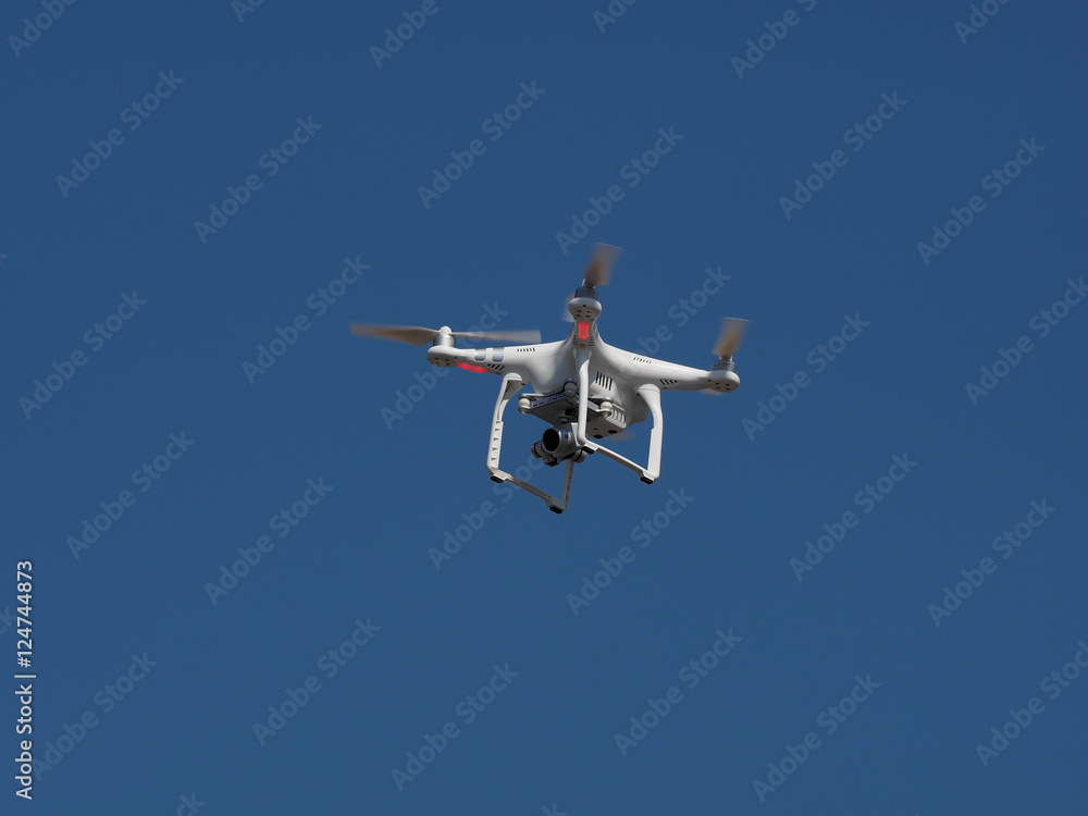 Underneath bottom view of a drone with stabilizer camera flying aerial overhead against a blue sky Underneath bottom view of a drone with stabilizer camera flying aerial overhead against a blue sky