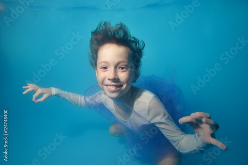 Little girl swims underwater in a white swimsuit with her hair, smiling and looking at me. Portrait. The view from the top. Close-up. Horizontal orientation