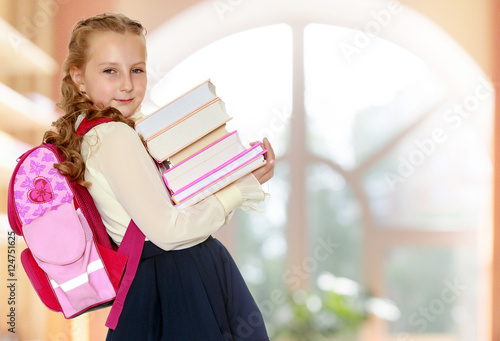 Girl schoolgirl with a satchel behind shoulders and books in han