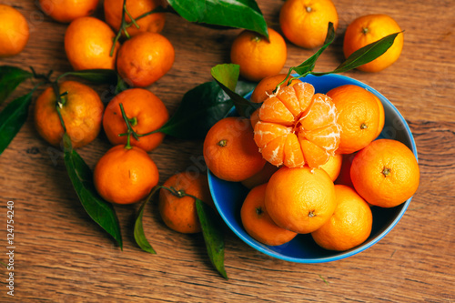 many fresh mandarin oranges in  blue bowl, standing on a wooden table