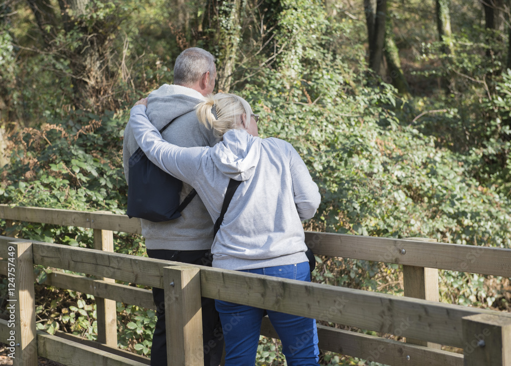 Fototapeta premium Mature couple standing on a bridge on a woodland area. 