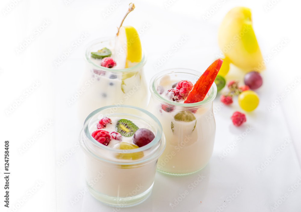 jars with yogurt and colorful fruits on a white background.