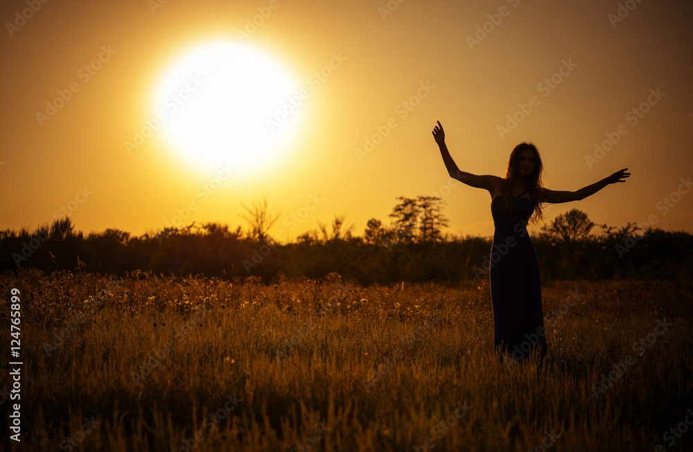 Silhouette of dancing young girl in dress against the sunset sky