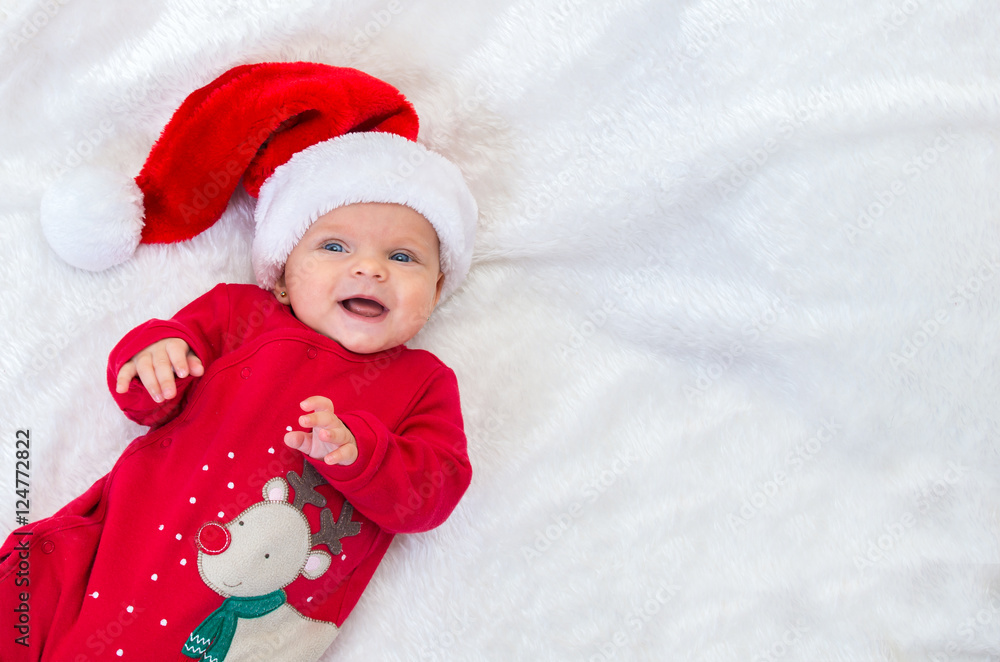 cheerful a baby girl with blue eyes in santa hat lying on a bed cheerful a baby girl with blue eyes in santa hat lying on a bed