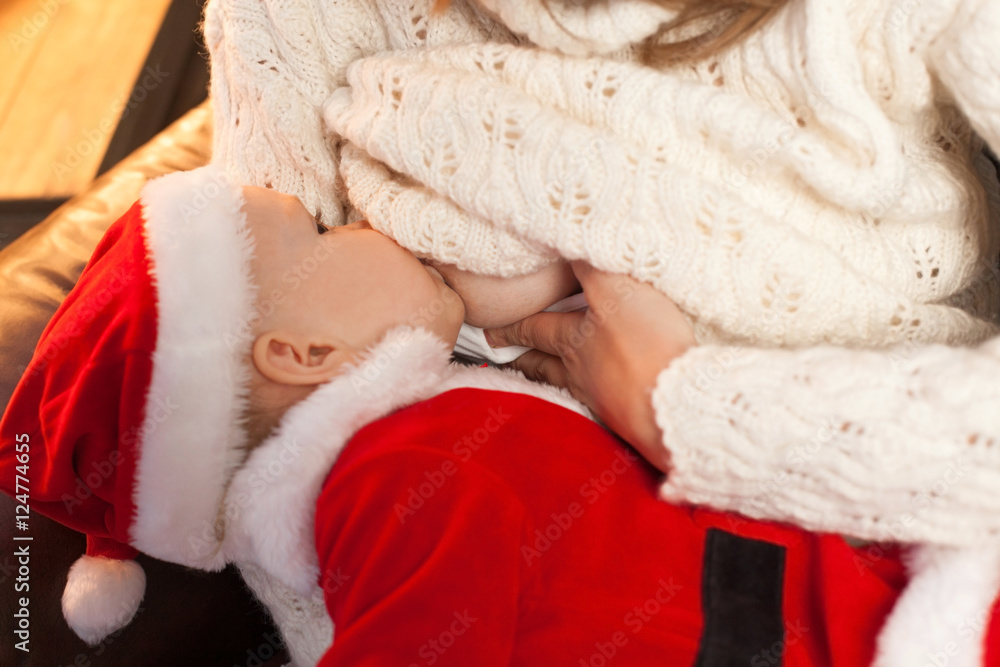 Newborn baby wearing as Santa Claus breast feeding. Selective focus on the kid s face. Homemade Christmas Newborn baby wearing as Santa Claus breast feeding. Selective focus on the kid s face. Homemade Christmas