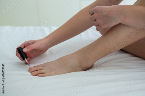 Woman applying nail polish on her toe nails in bedroom