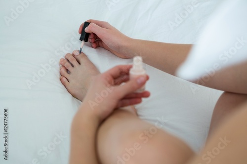 Woman applying nail polish on her toe nails in bedroom