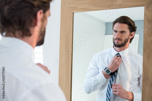 Obraz na plátne Man getting dressed in bedroom while looking at mirror