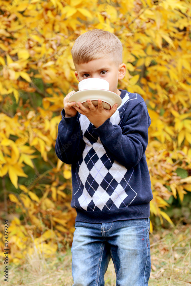 Handsome small boy holds a coffee cup and plate outdoors. Handsome small boy holds a coffee cup and plate outdoors.