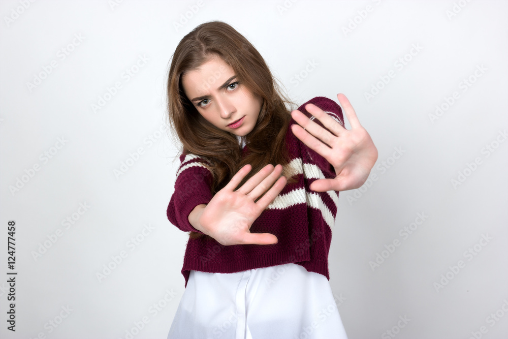 Portrait of a pretty woman in short sweater shirt showing stop with, white two hands standing over gray background and looking at camera Portrait of a pretty woman in short sweater shirt showing stop with, white two hands standing over gray background and looking at camera