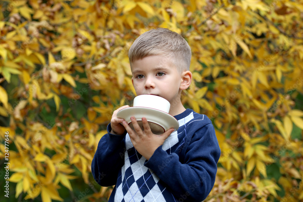 Handsome small boy holds a coffee cup and plate outdoors. Handsome small boy holds a coffee cup and plate outdoors.