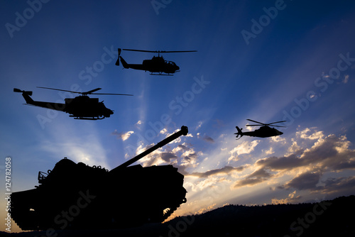 Military tank and helicopters silhouetted against dawn or dusk blue sky