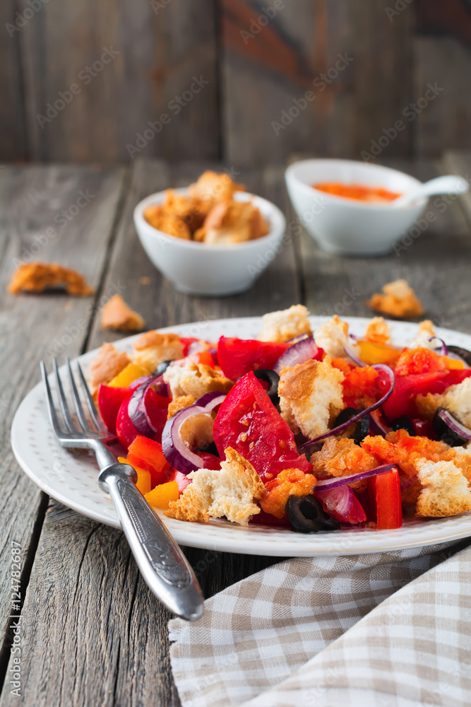 Salad with peppers, tomatoes, onions, olives and croutons with sauce old wooden background. Selective focus.