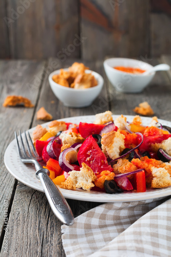 Salad with peppers, tomatoes, onions, olives and croutons with sauce old wooden background. Selective focus.