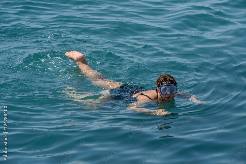 Mature woman is swimming with swim mask in the sea.