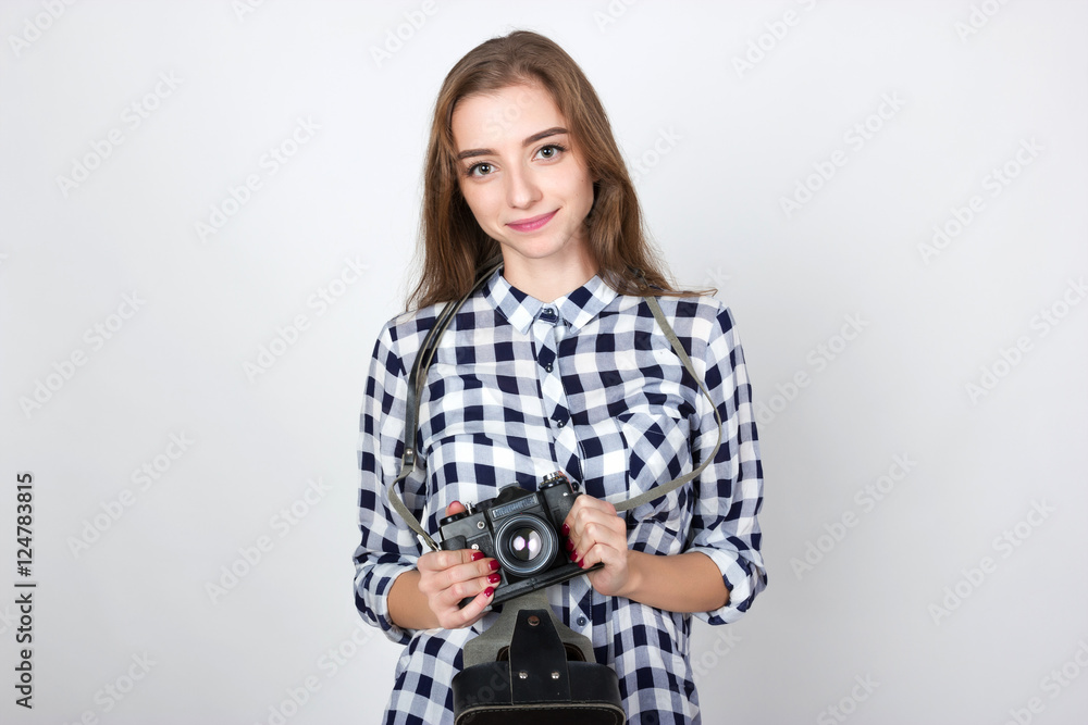 Portrait of a pretty smiling woman in plaid shirt holding an old camera in hands standing over gray background and looking at camera Portrait of a pretty smiling woman in plaid shirt holding an old camera in hands standing over gray background and looking at camera