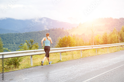 Young athletic woman jogging on road in mountains