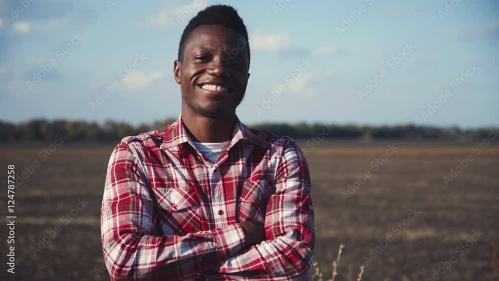 Cheerful african guy in plaid shirt standing in field with arms crossed and looking at camera. Cheerful african guy in plaid shirt standing in field with arms crossed and looking at camera.