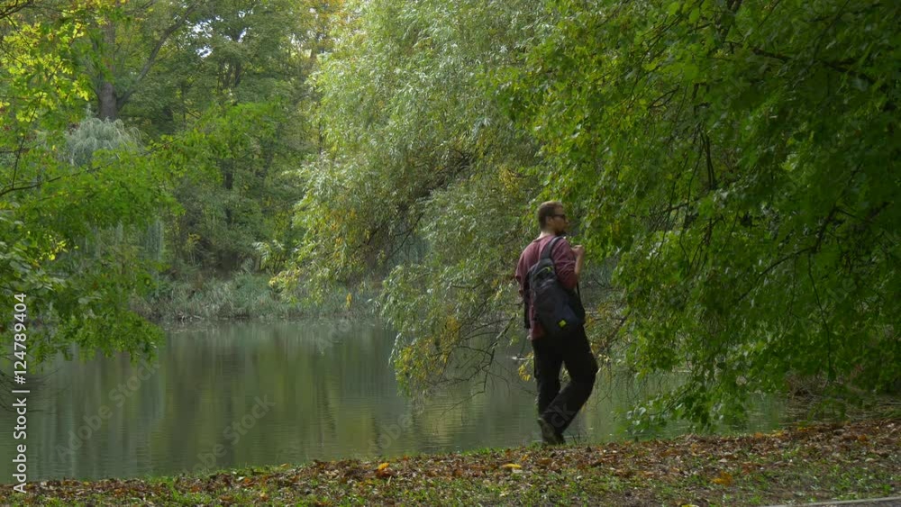 Backpacker Comes Sits Down at the Lake Bank Park Forest Walking and Looking at Smooth Water Resting Outdoors Dry Leaves on a Ground Autumn Landscape Backpacker Comes Sits Down at the Lake Bank Park Forest Walking and Looking at Smooth Water Resting Outdoors Dry Leaves on a Ground Autumn Landscape