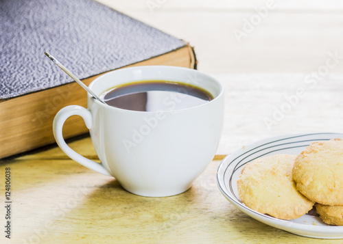 a cup of black coffee with cookies and book on wooden table