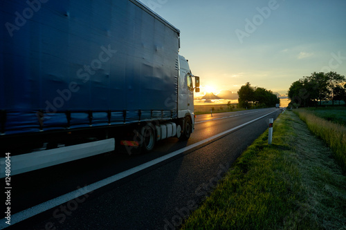 Obraz na płótnie Truck driving on asphalt road towards the horizon in rural landscape at sunset. w salonie