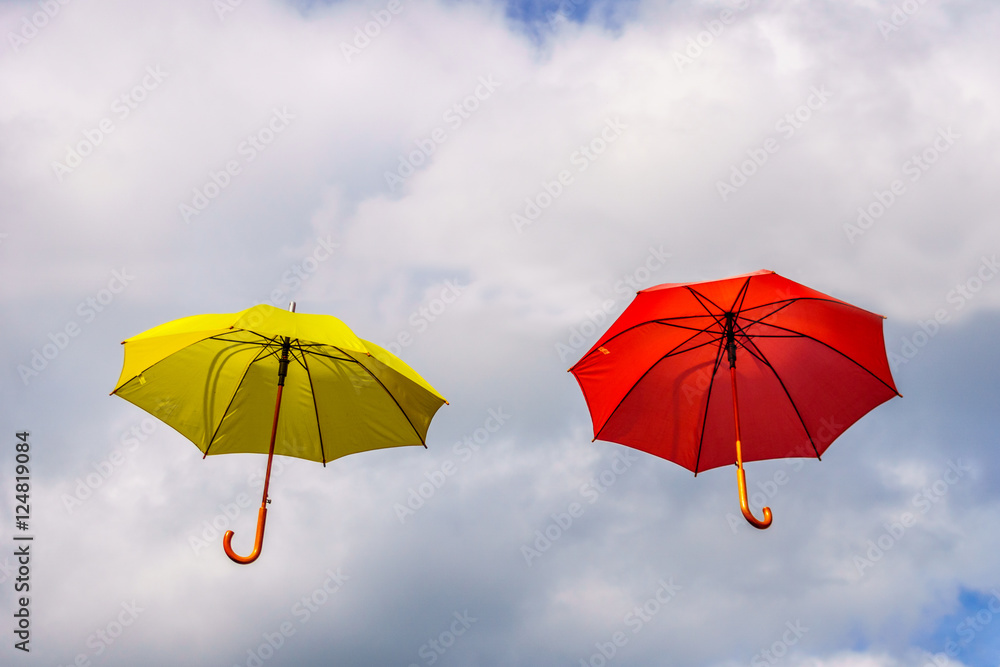 Yellow and red umbrella or parasols floating suspended in the air under cloudy sky