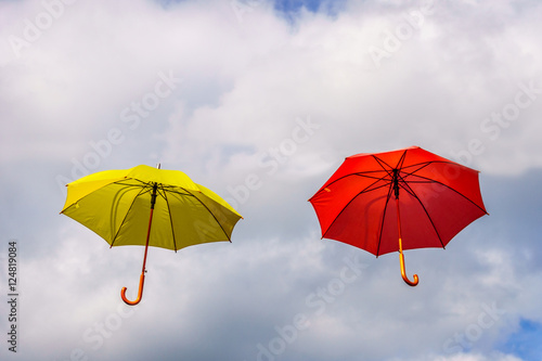 Yellow and red umbrella or parasols floating suspended in the air under cloudy sky