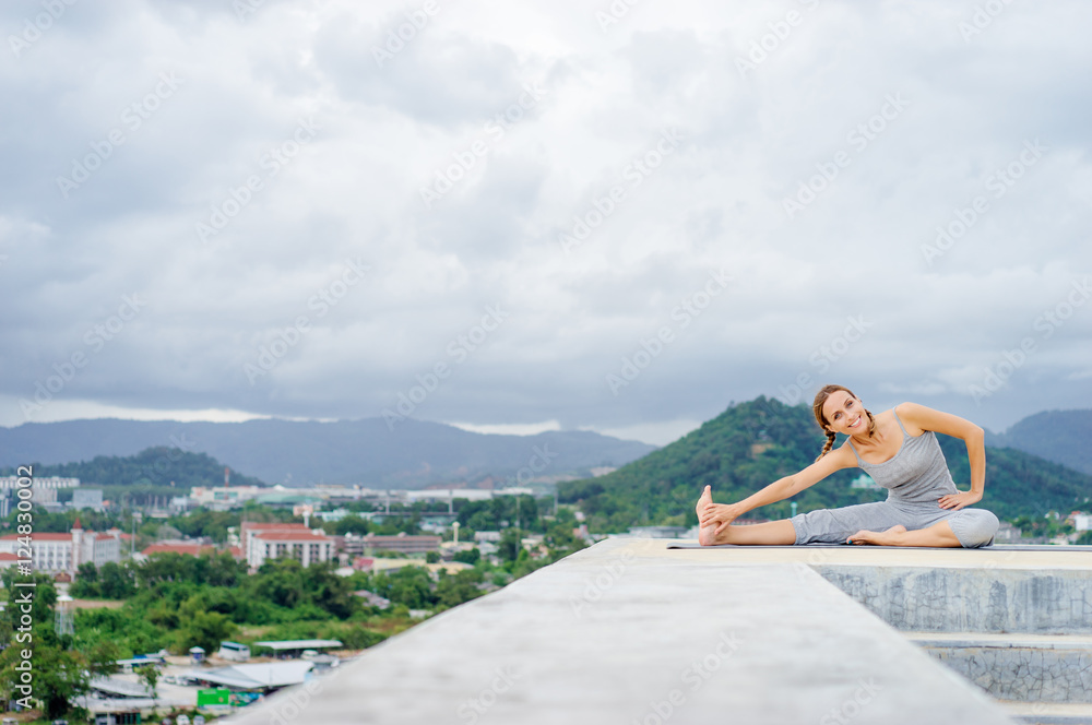 Yoga on rooftop. Happy young woman stretching on roof with city and mountains view.