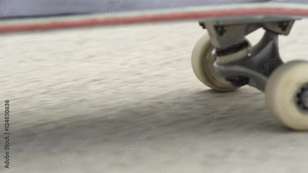 CLOSE UP Skateboard deck and wheels spinning along the concrete street