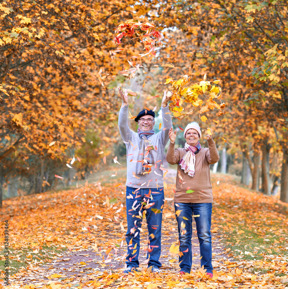 Fototapeta premium lachendes Seniorenpaar in einer Allee, Laub werfen im Herbst