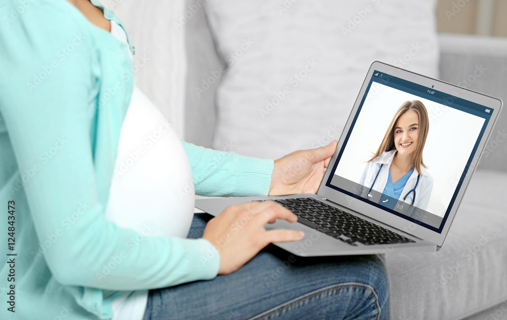 Fototapeta premium Pregnant woman video chatting with doctor on laptop. Professional medical online consultation concept.