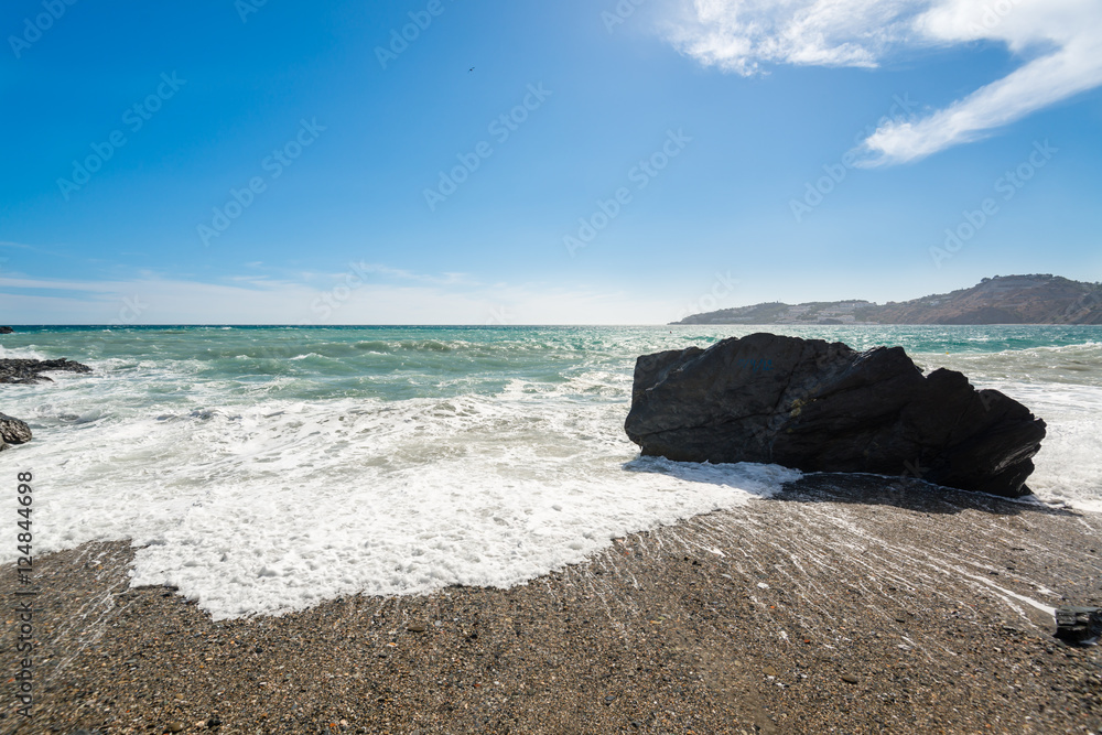 A day view of a spanish mediterranean beach with a rock in a side