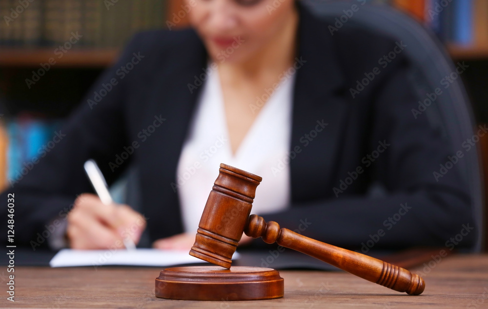Brown gavel on wooden table and female lawyer on background, close up view Brown gavel on wooden table and female lawyer on background, close up view
