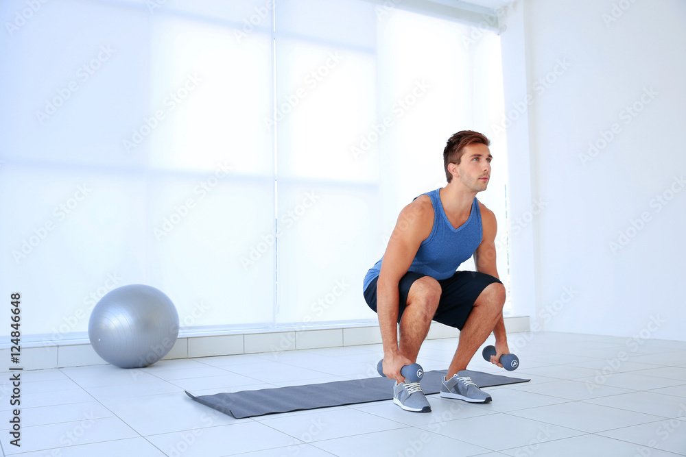 Young man doing exercises with dumb-bells on rug indoor Young man doing exercises with dumb-bells on rug indoor