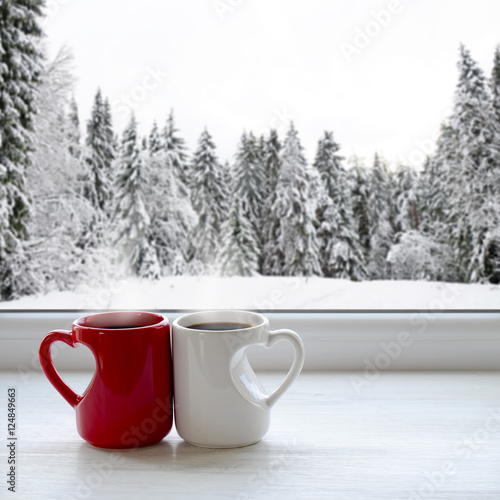Two cups of coffee on a windowsill. In the background, a beautiful winter forest in snow
