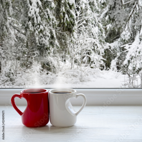 Two cups of coffee on a windowsill. In the background, a beautiful winter forest in snow