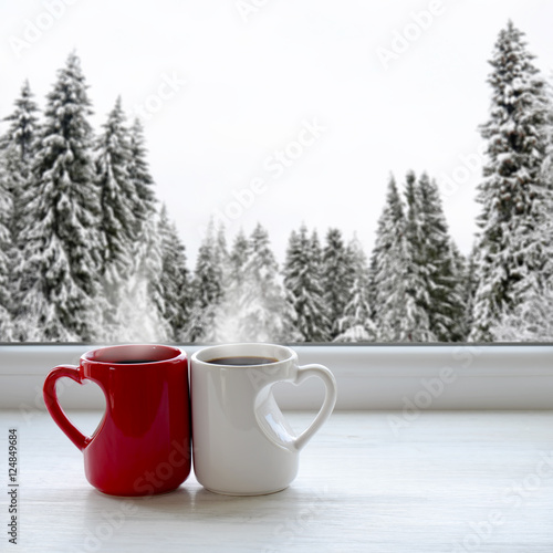 Two cups of coffee on a windowsill. In the background, a beautiful winter forest in snow