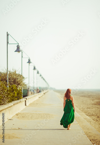 Lonely woman in green dress walks along the coast under grey lan © pyrozenko13