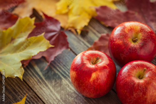 Red autumn apples with maple leaves on wooden table